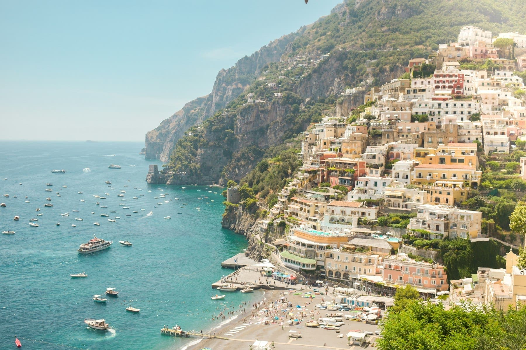 Pastel houses of Positano stacked above a beach and boats on the Amalfi Coast