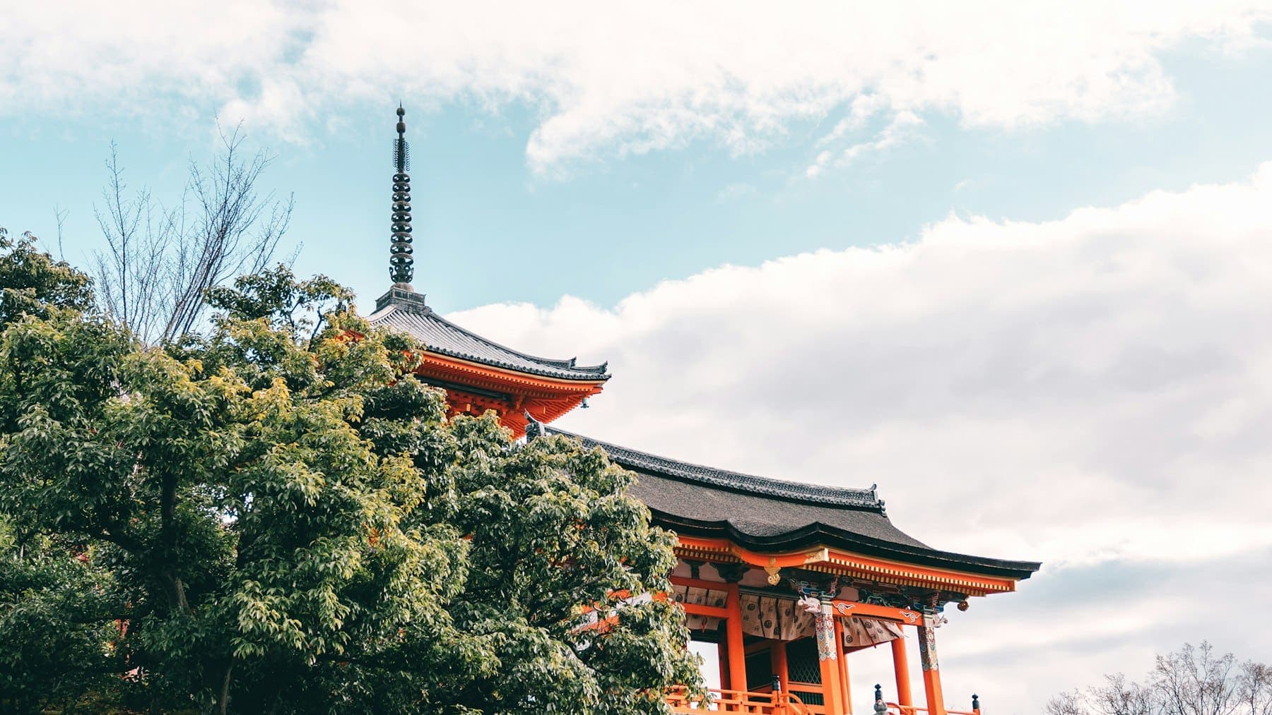 Vermilion pagoda of Kiyomizu-dera temple rising above green trees in Kyoto